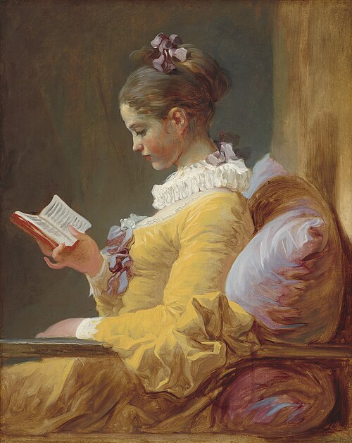 Young woman in yellow-saffron dress with a frilly neckline reading a book in a comfy chair